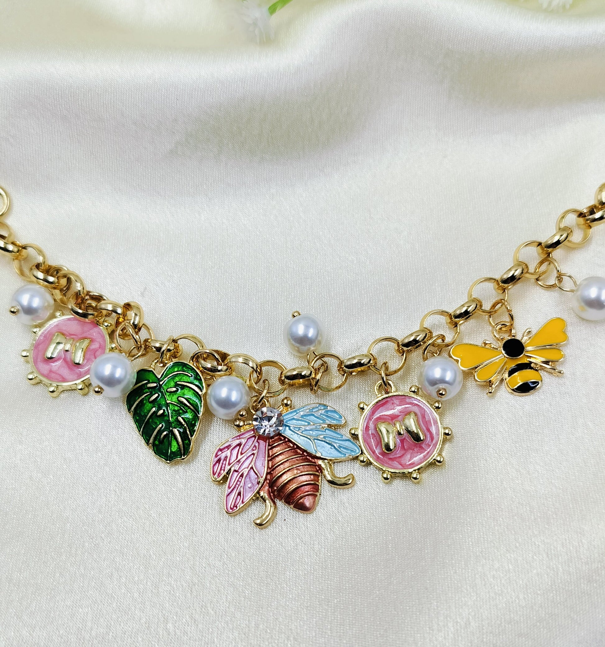 Gold charm bracelet with colorful butterfly, bee, leaf, and pearl charms, trendy women's jewelry on fabric background