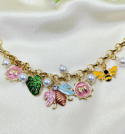 Gold charm bracelet with colorful butterfly, bee, leaf, and pearl charms, trendy women's jewelry on fabric background