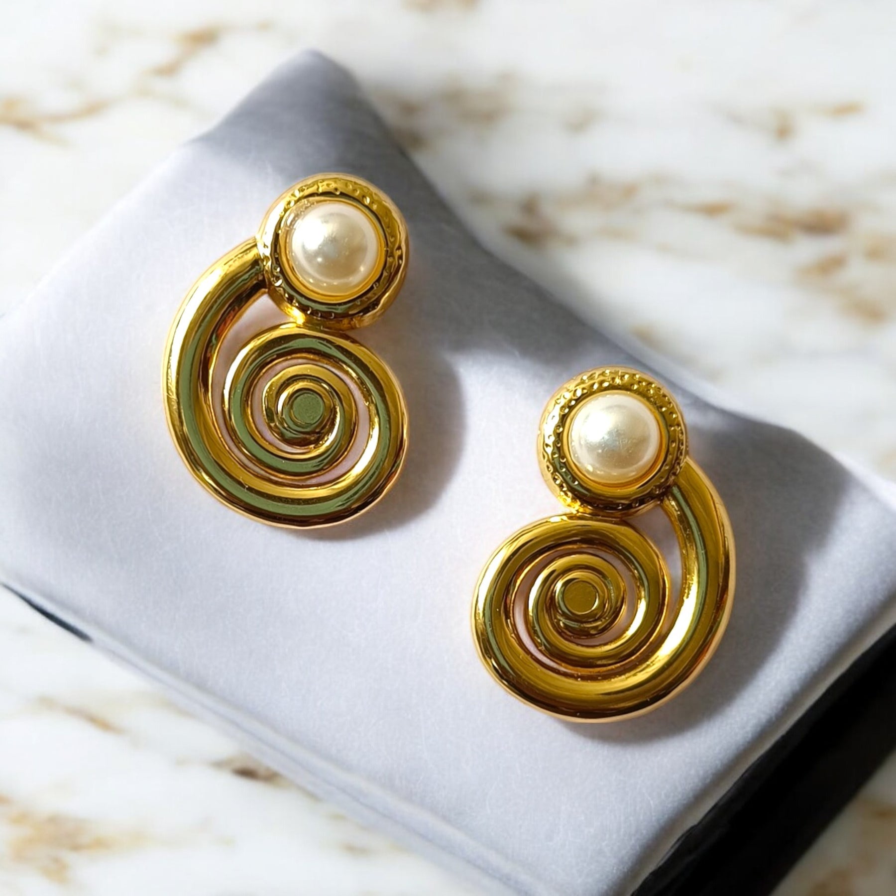 Gold spiral earrings with pearl accents on a gray cushion.