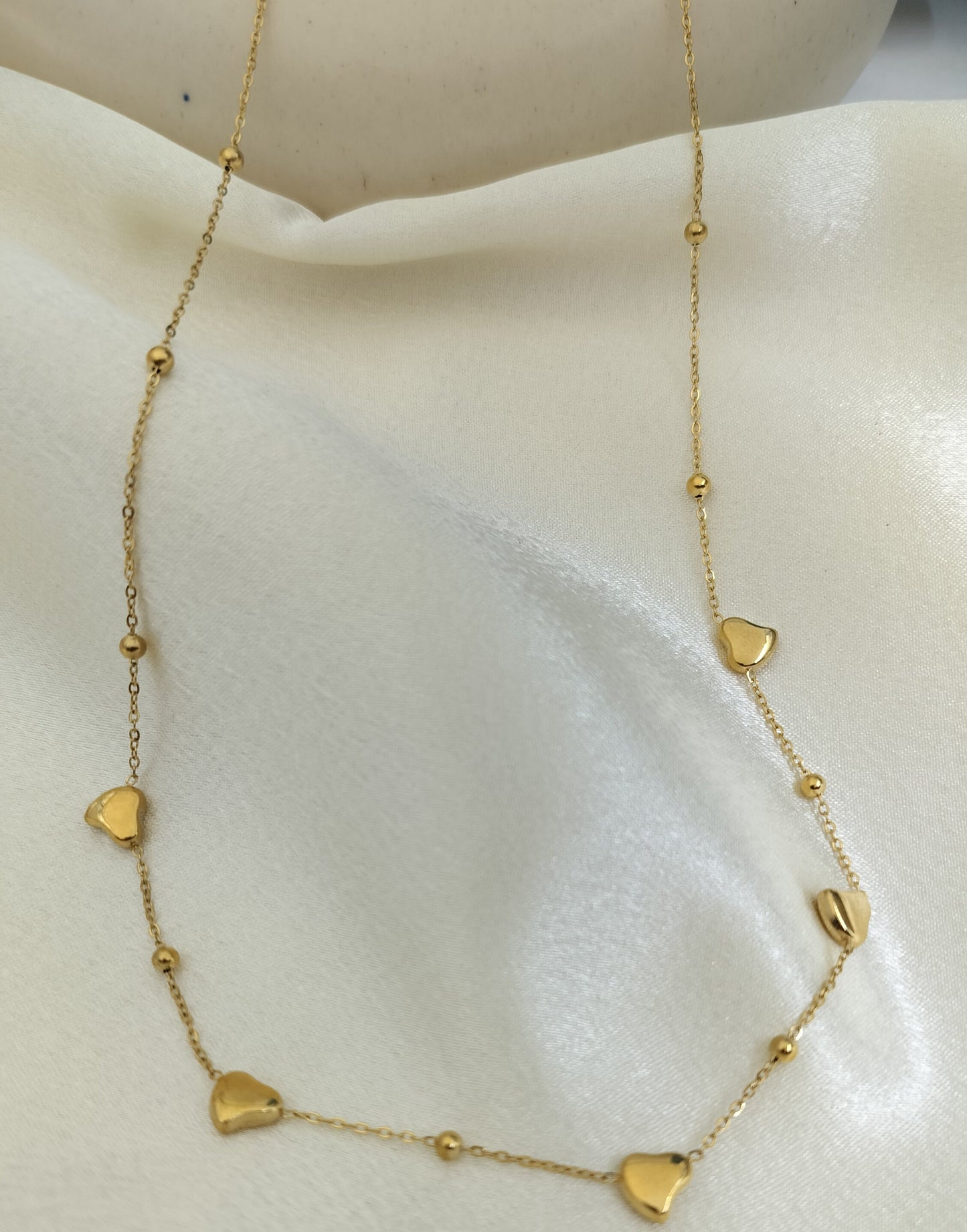 Elegant gold chain necklace with small heart charms and bead accents displayed on white fabric.