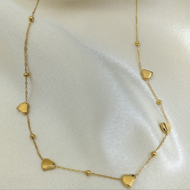 Elegant gold chain necklace with small heart charms and bead accents displayed on white fabric.