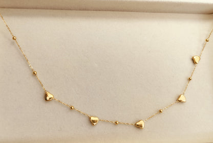Delicate gold chain necklace with small heart charms and bead accents displayed on beige background.