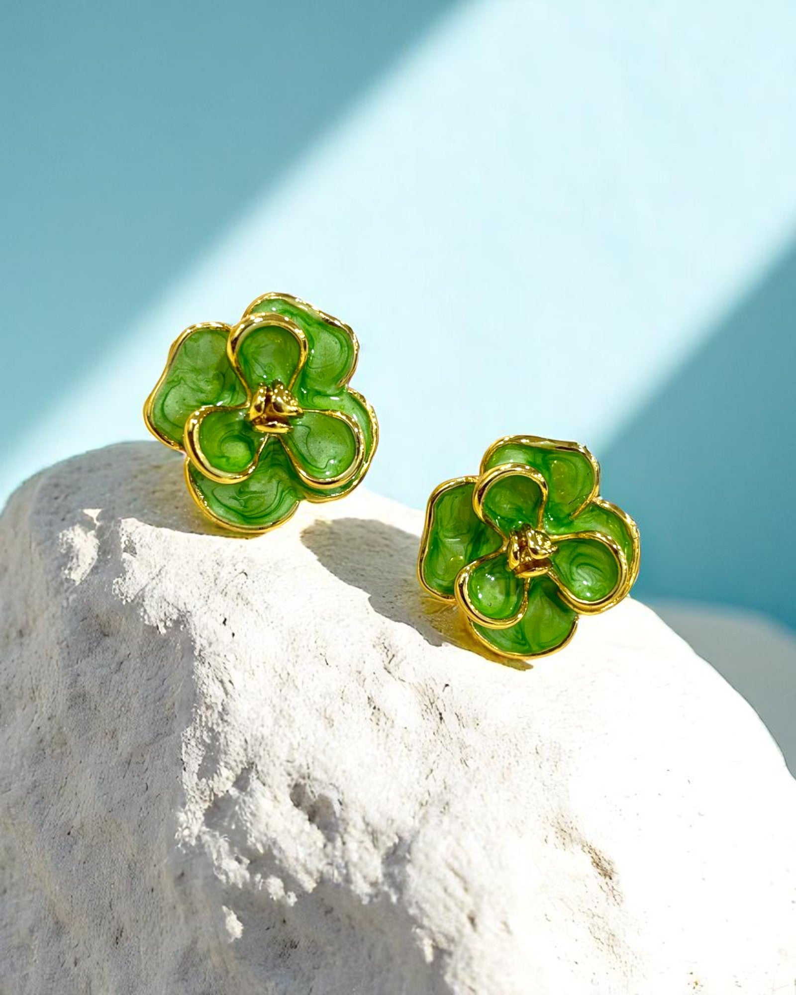 Gold plated floral stud earrings with glossy green enamel petals placed on a white stone – Glampouch jewelry