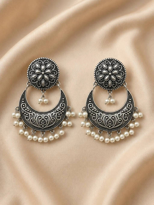 Pair of oxidised silver chandbali earrings with pearl drops laid flat on cream satin fabric