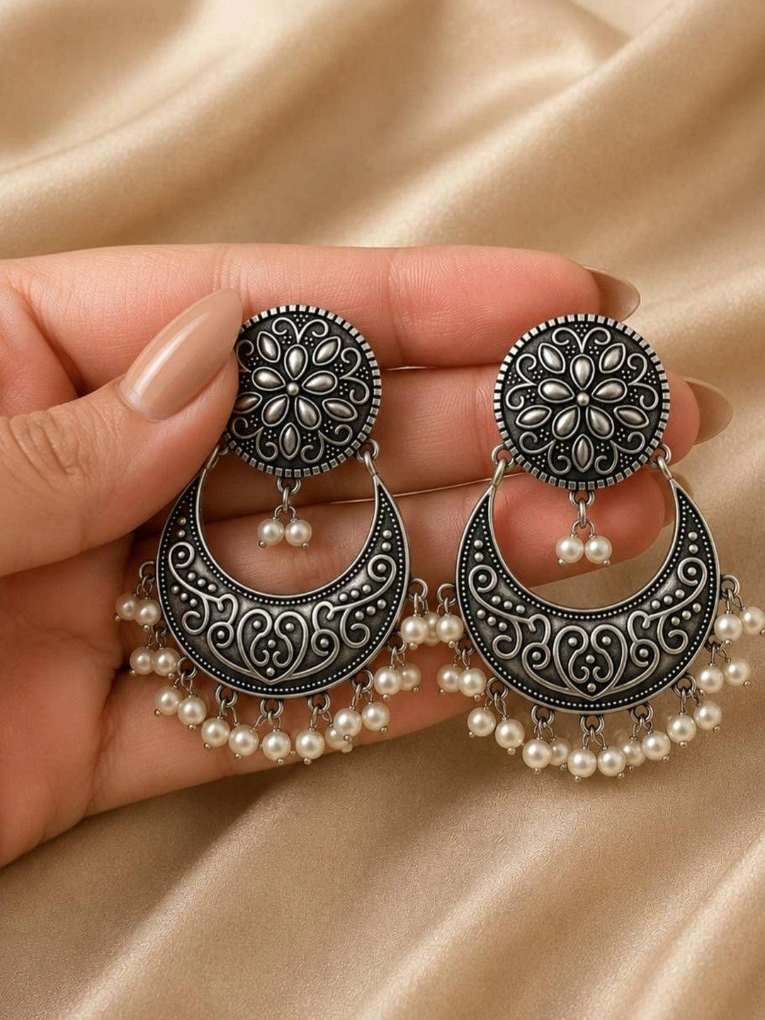 Both chandbali earrings held in a model hand displaying engraved scrollwork and pearl fringe