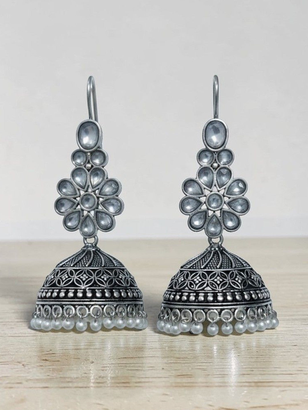 Pair of oxidised silver kundan jhumka earrings with pearl drops resting on a wooden surface