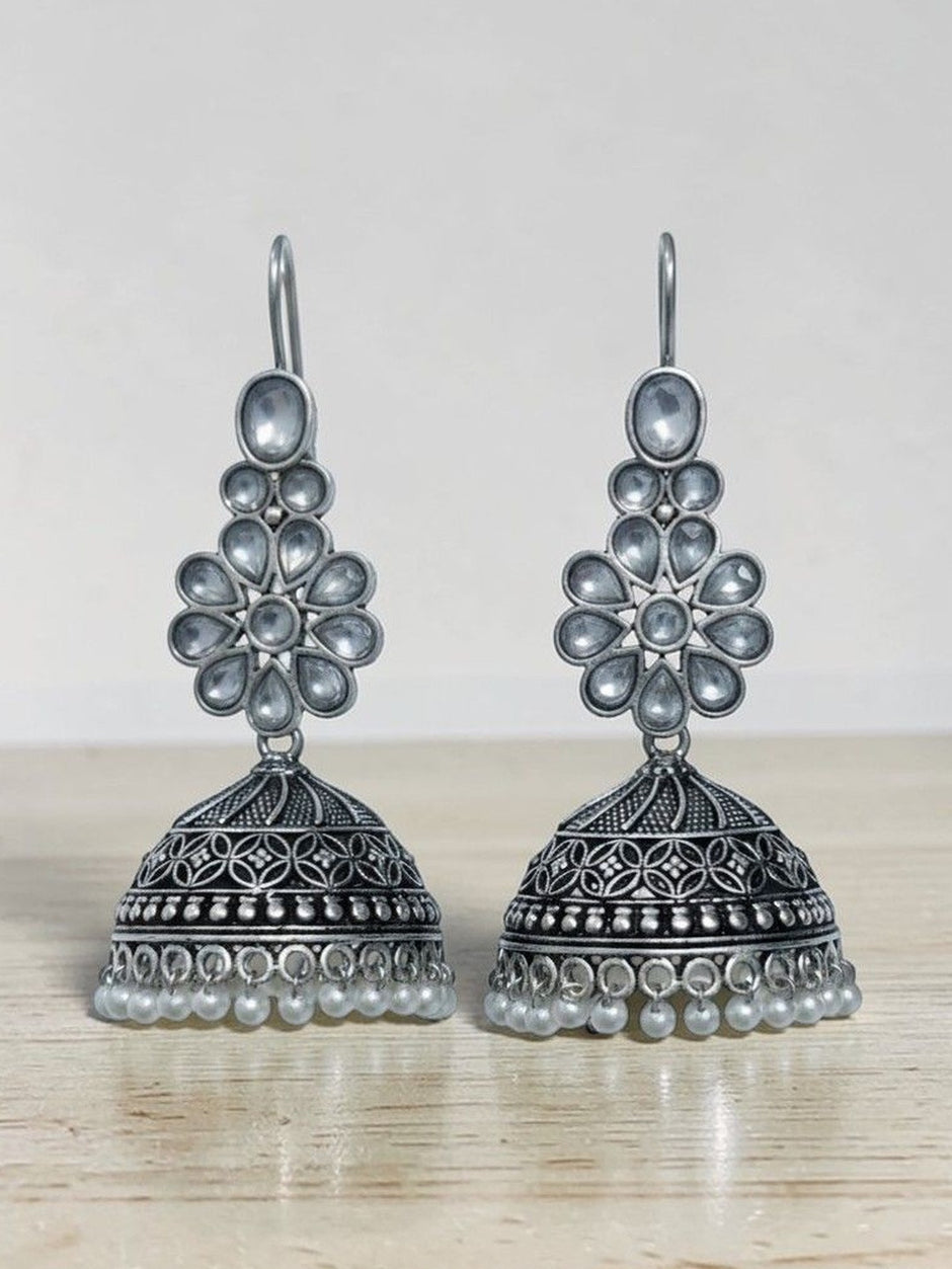 Pair of oxidised silver kundan jhumka earrings with pearl drops resting on a wooden surface