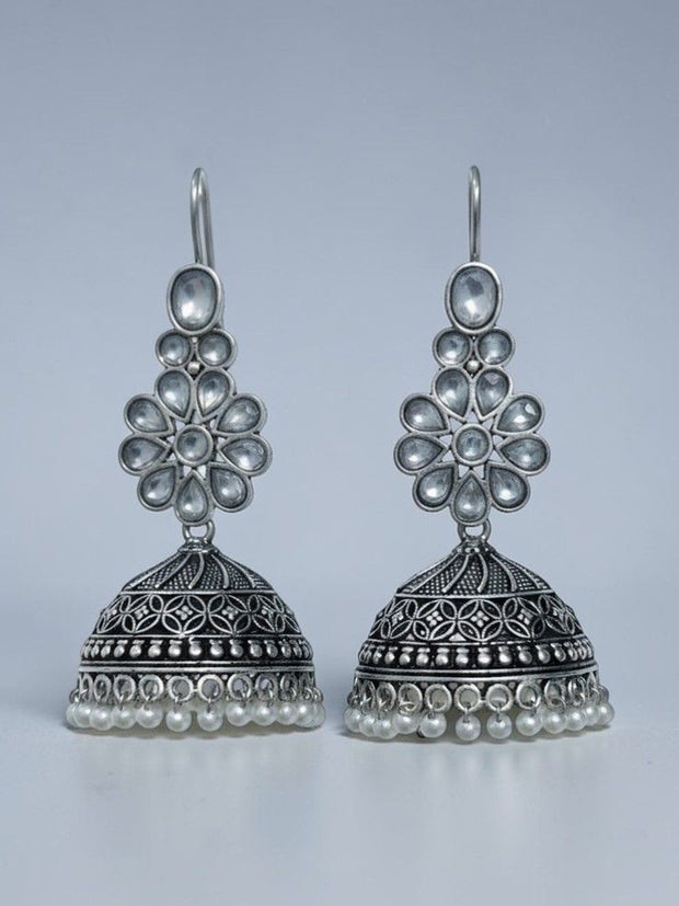Front view of oxidised silver floral kundan jhumka earrings with engraved dome and pearl fringe on grey background