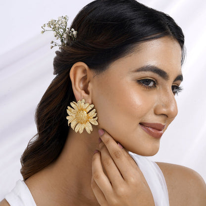 Beautiful woman wearing oversized floral gold statement earrings, styled with soft makeup and elegant hair adorned with delicate flowers – a perfect festive and bridal jewelry look.