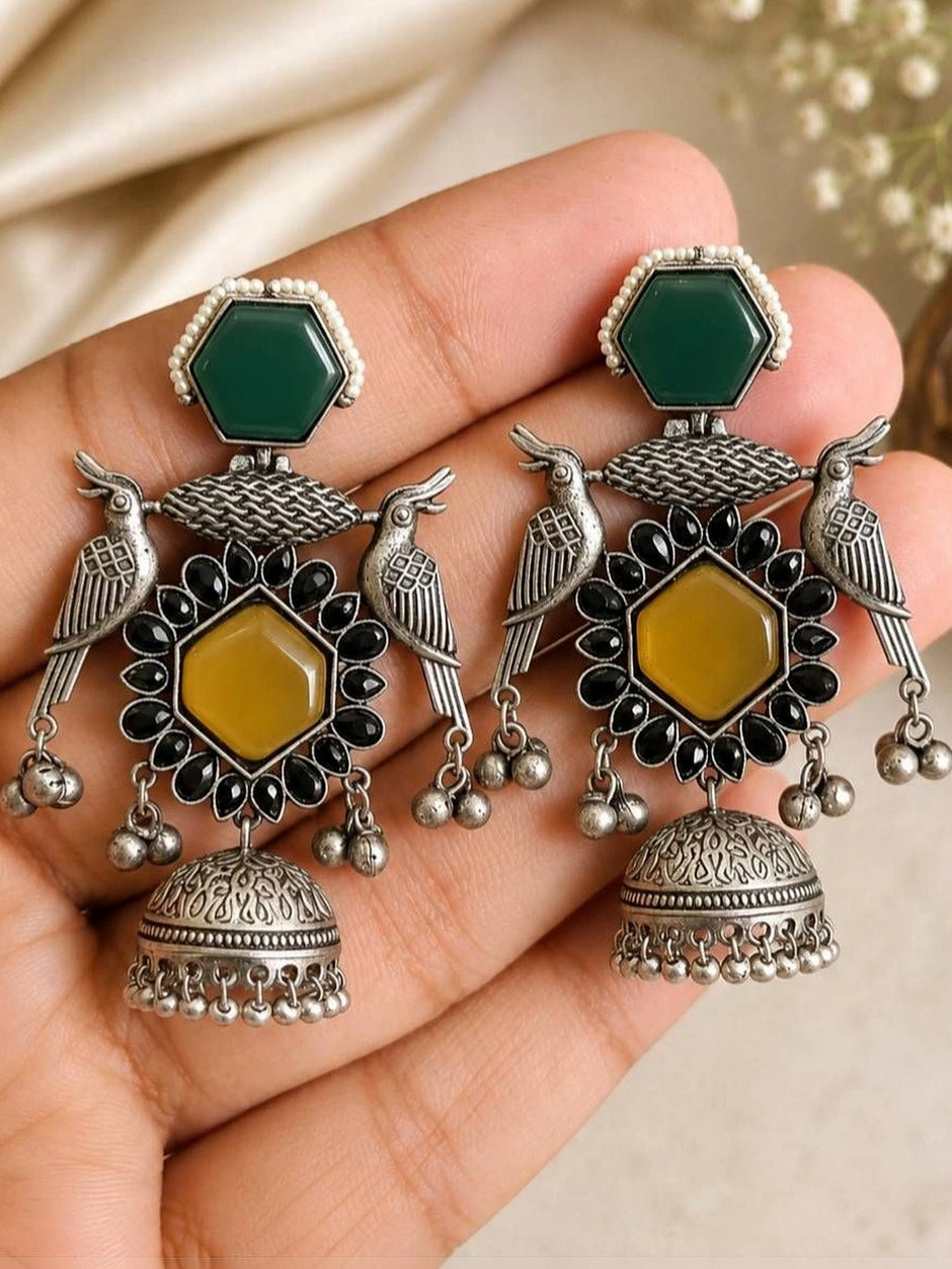 Close-up of two oxidised silver bird jhumka earrings with black stone accents and ghungroo drops held in a palm