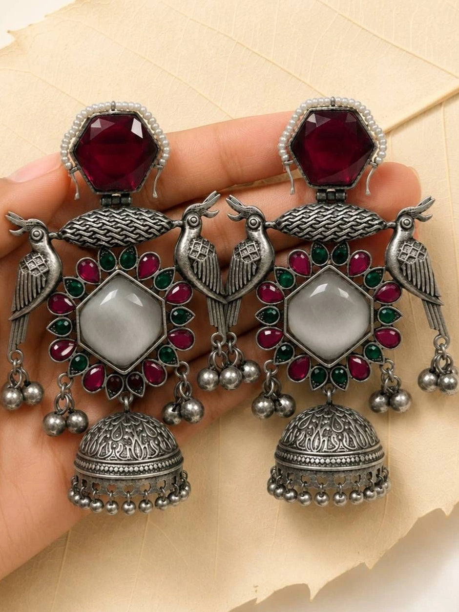 Both oxidised silver peacock jhumka earrings held in a woman's palm showing full intricate detail