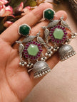 Both oxidised silver peacock jhumka earrings resting on a woman's open palm showing engraved dome and pearl drops