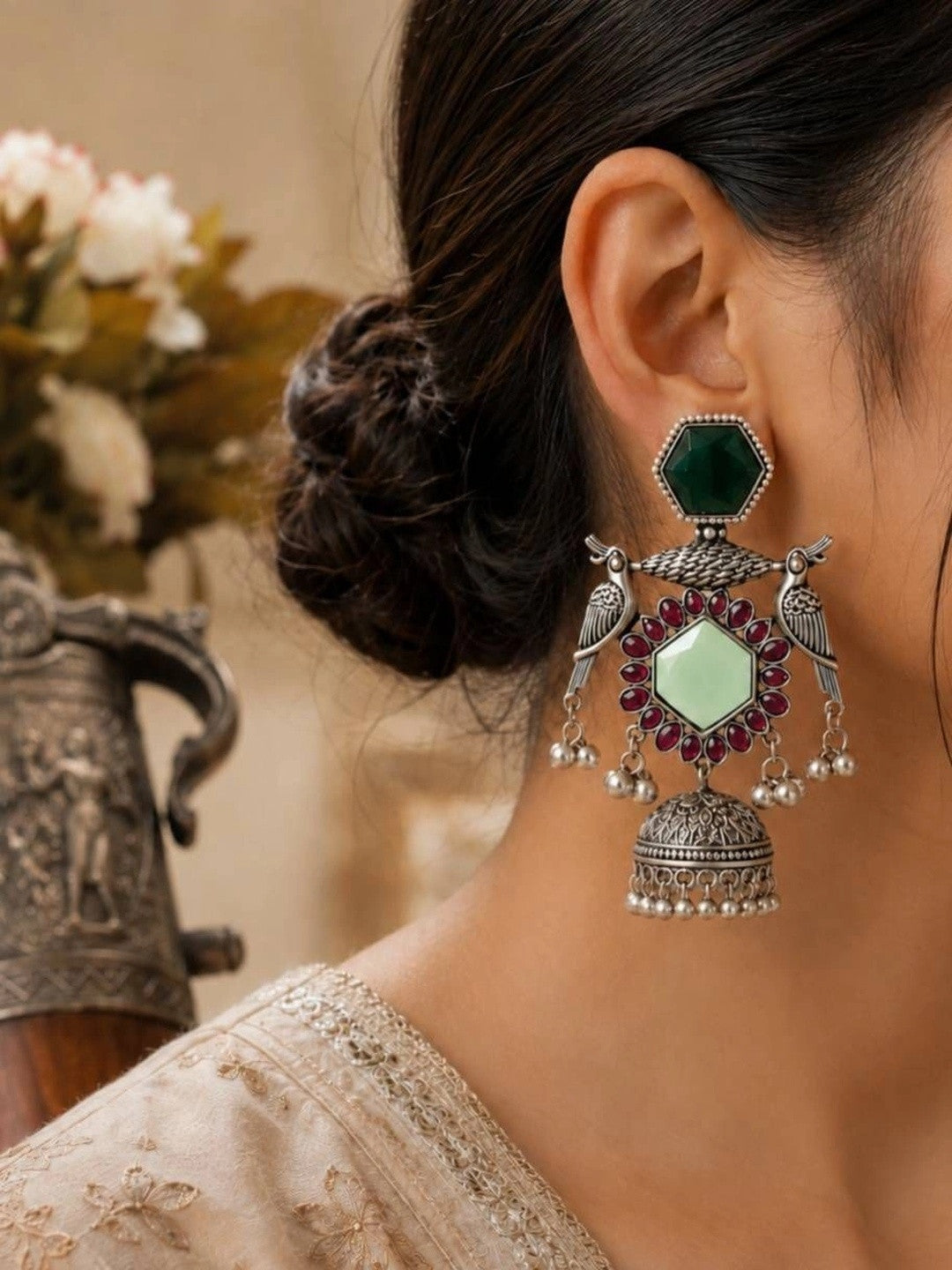 Oxidised silver peacock jhumka earring worn on a woman's ear styled with an ivory embroidered blouse and hair in a bun
