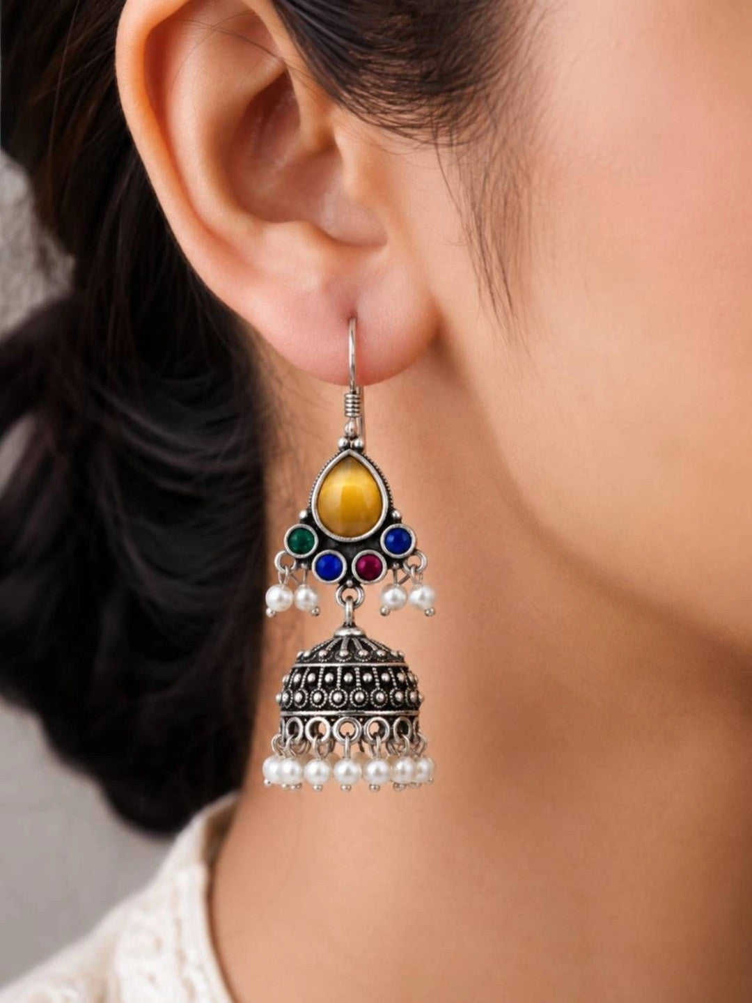 Close-up side view of oxidised silver multicolour stone jhumka earring worn on a woman's ear