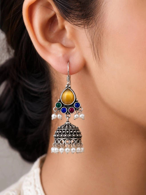 Close-up side view of oxidised silver multicolour stone jhumka earring worn on a woman's ear
