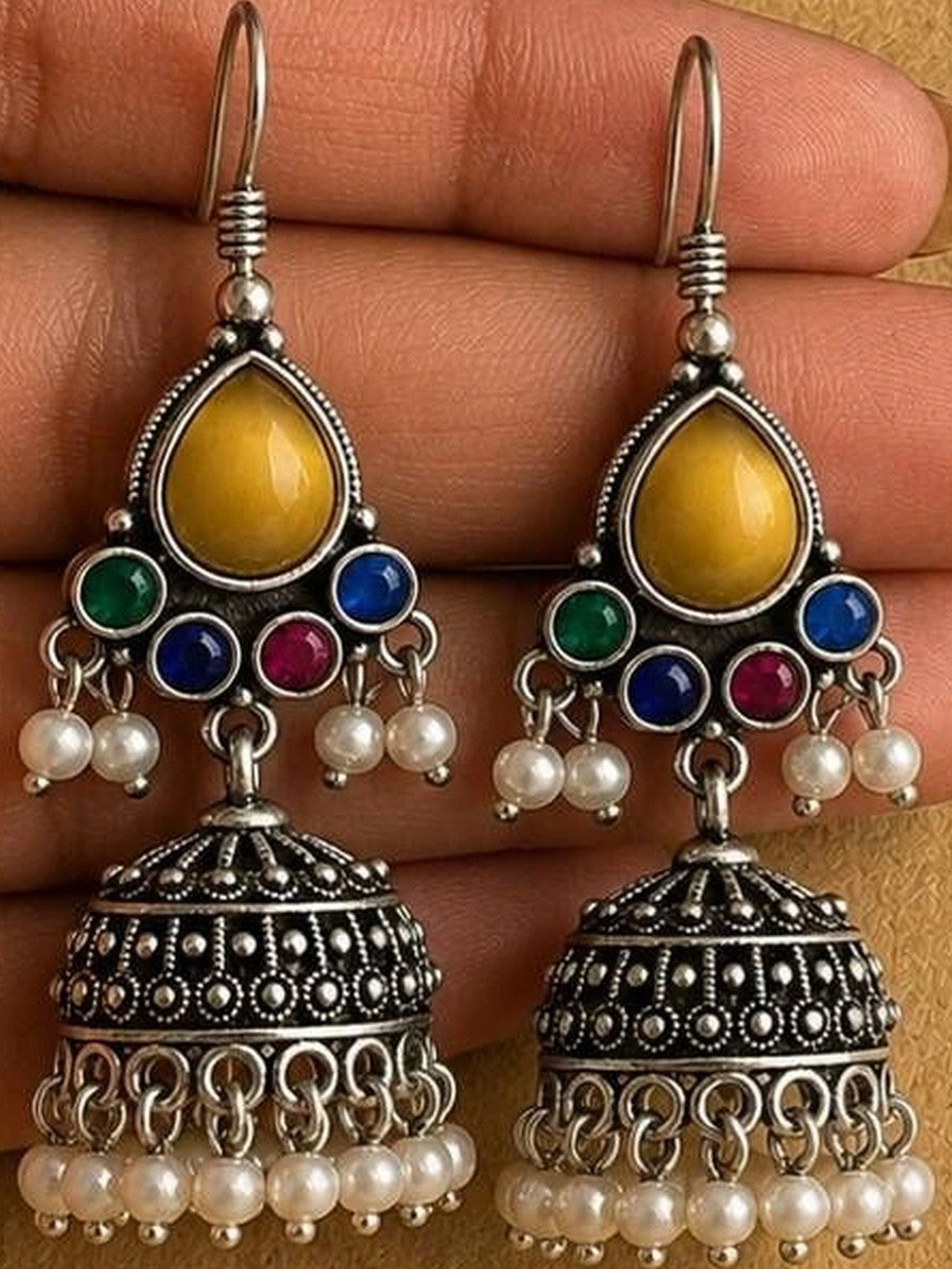 Pair of oxidised silver jhumka earrings with pearl drops held in a woman's open palm showing detailed dot and scroll work