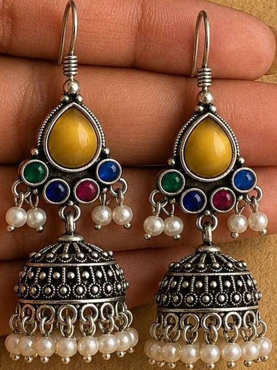 Pair of oxidised silver jhumka earrings with pearl drops held in a woman's open palm showing detailed dot and scroll work