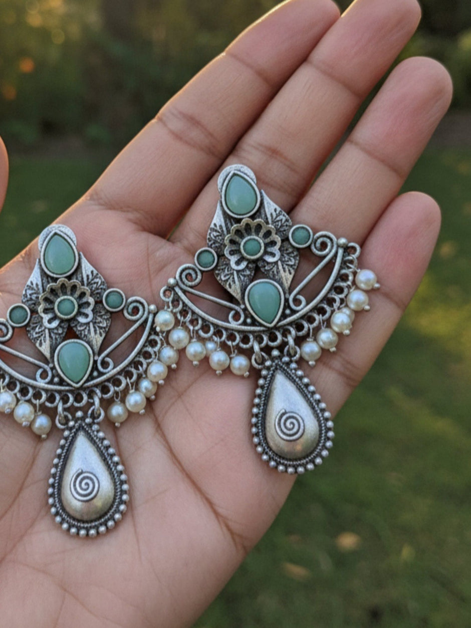 Both oxidised silver turquoise earrings held in an open palm showing front detail and pearl drops outdoors