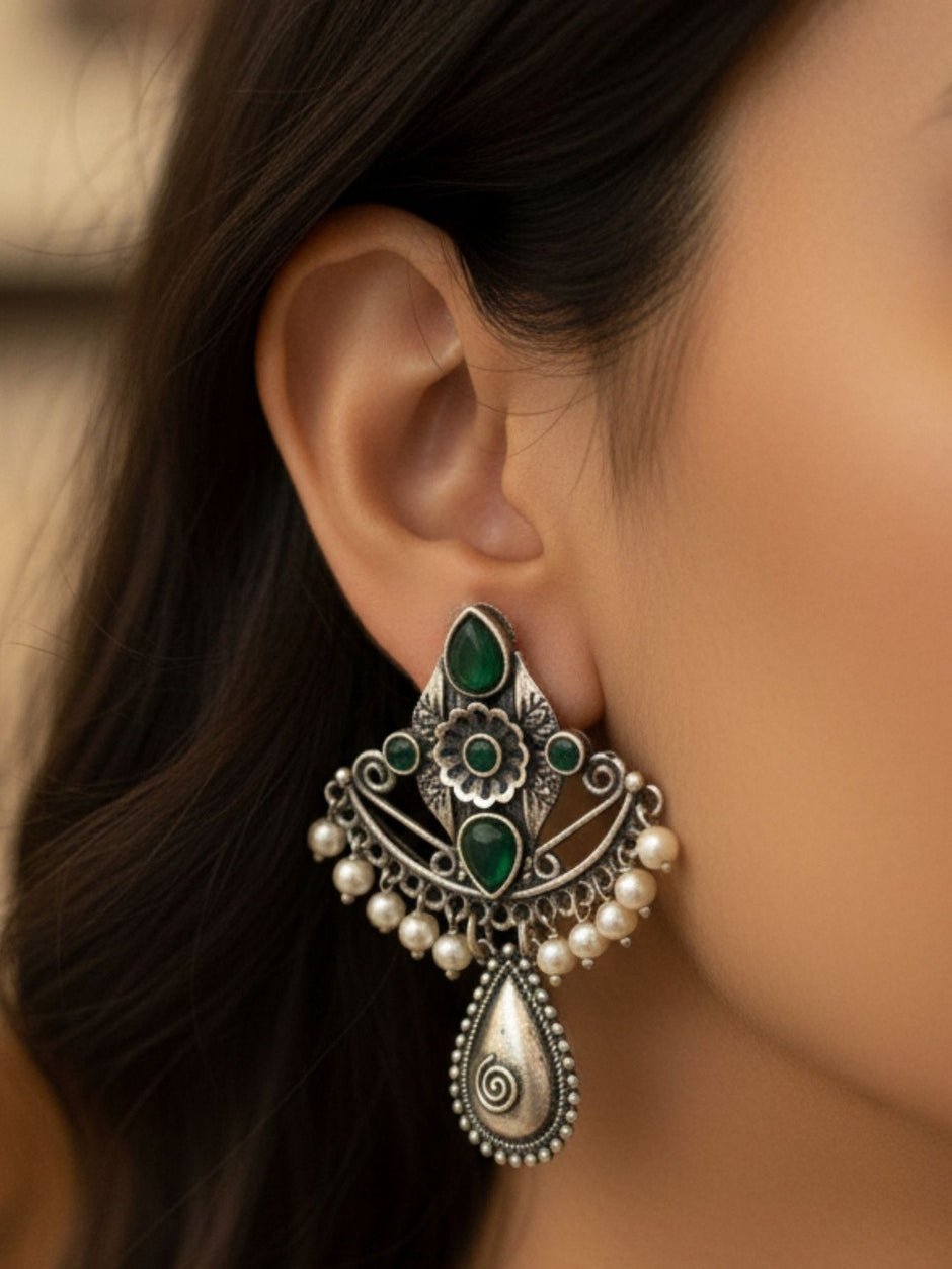 Oxidised silver chandbali earring with green stones worn on a woman's ear against dark hair