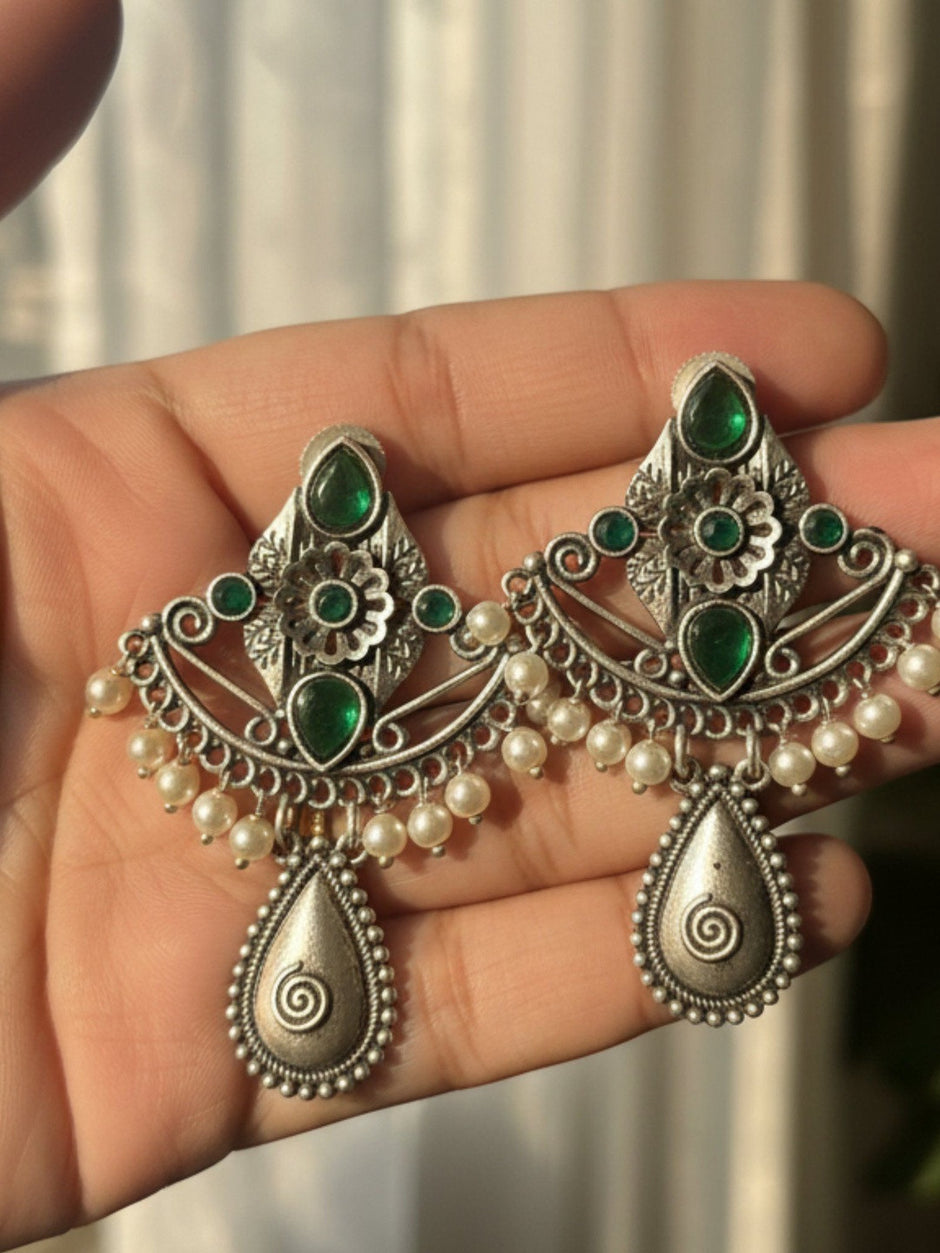 Both oxidised silver chandbali earrings with green stones and pearl drops resting on an open palm