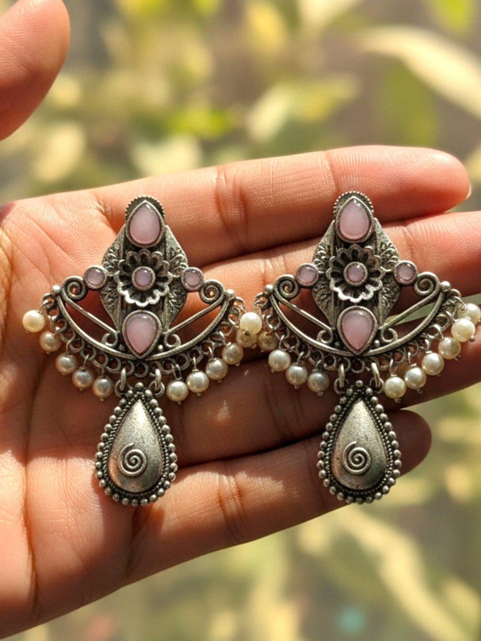 Pair of oxidised silver chandbali earrings with pink stones and pearl beads held in a palm against a green outdoor background