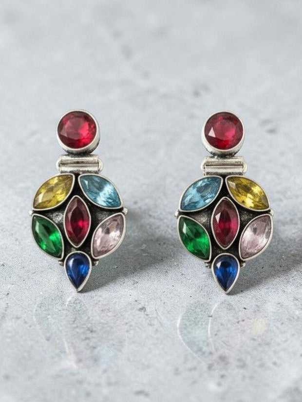 Close-up of oxidised silver multi-stone drop earrings showing red, blue, green and yellow crystals on grey background