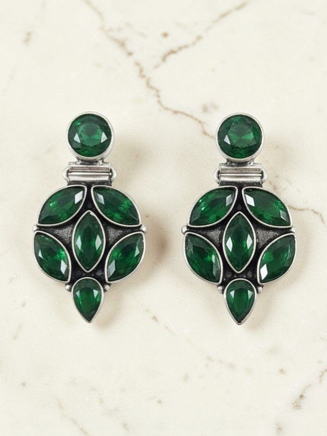 Pair of oxidised silver drop studs with emerald green marquise and round stones on marble surface