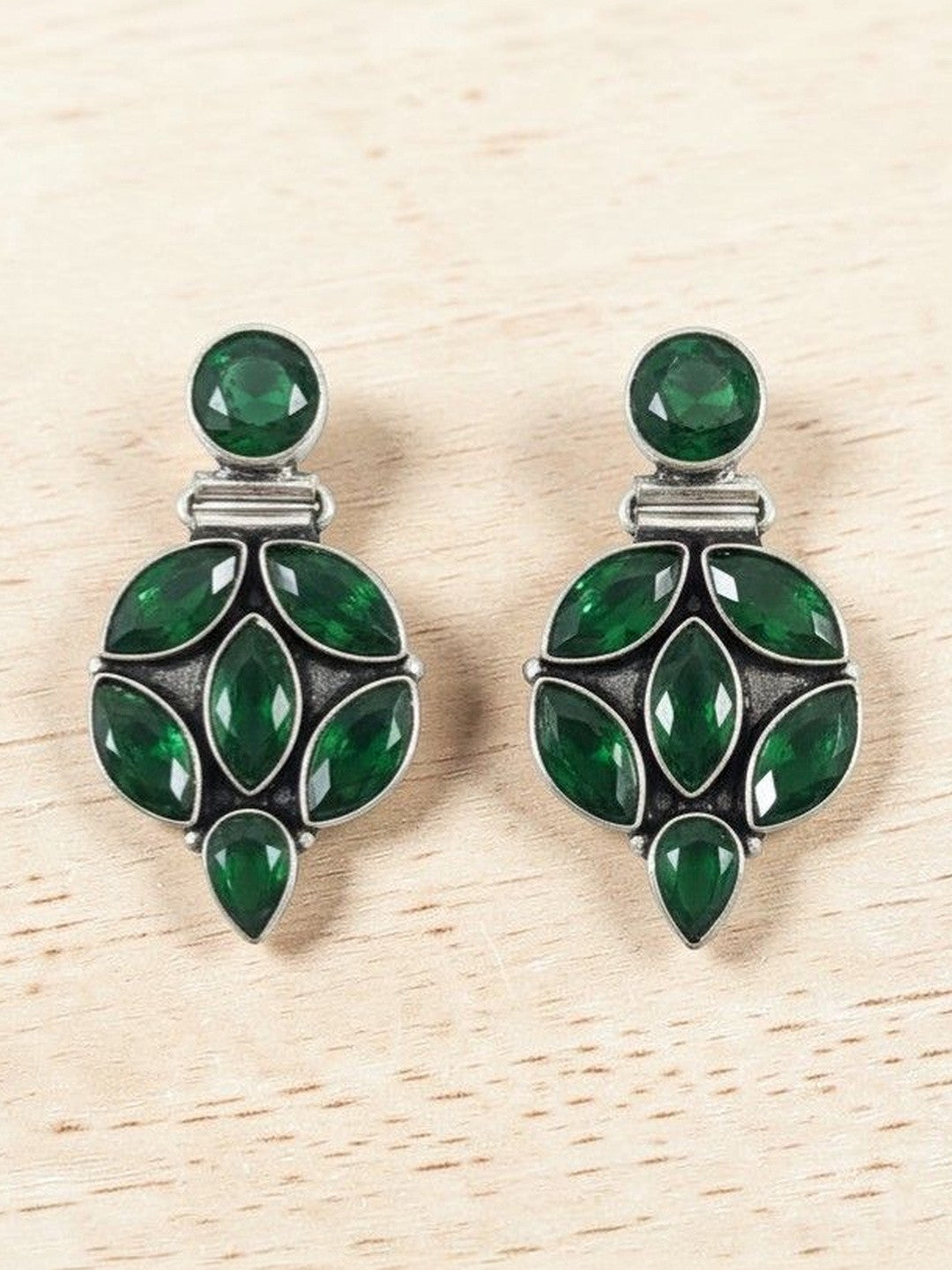Front view of green stone oxidised silver cluster earrings displayed on a light wood background
