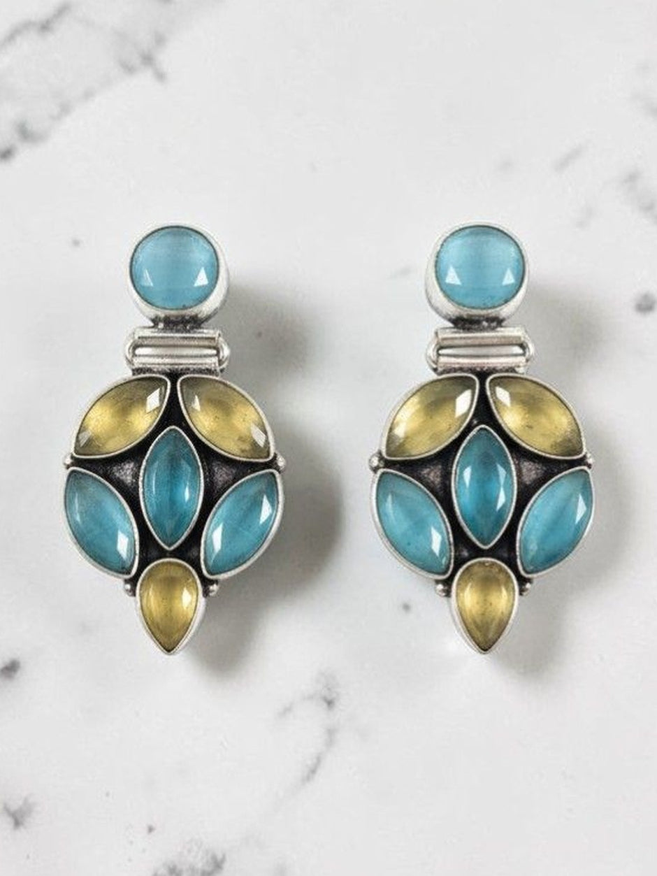 Pair of oxidised silver drop earrings with blue and yellow-green stone clusters on a marble background