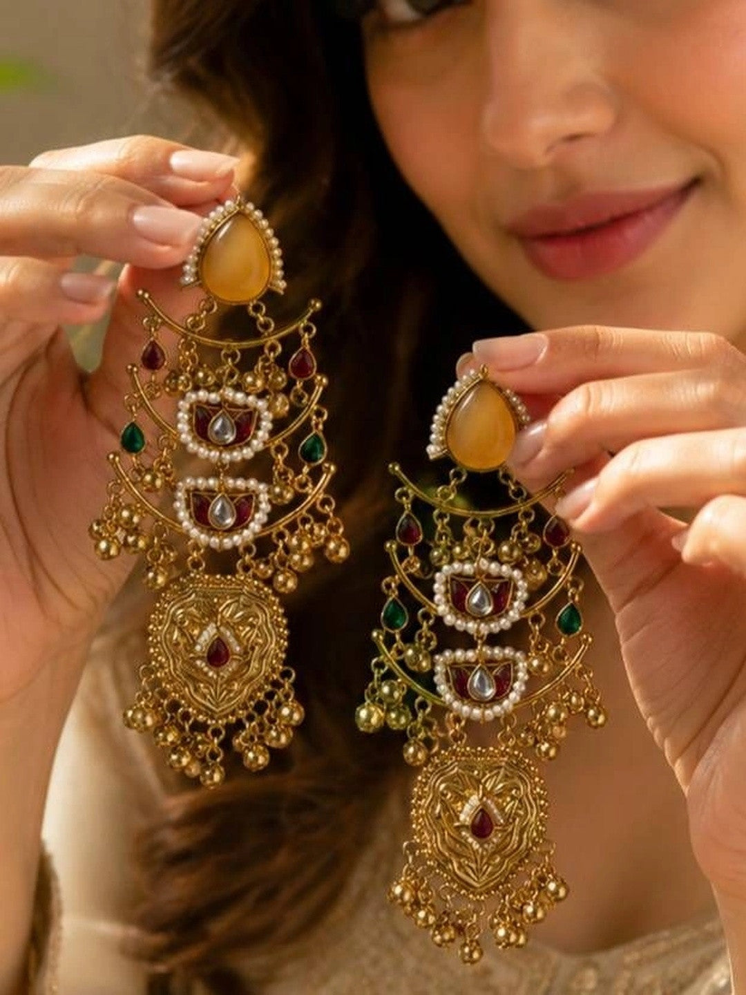 Woman holding both gold kundan chandbali earrings up close to show tiers and ghungroo bells