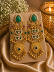 Pair of gold-plated kundan chandbali earrings with emerald green stones and ghungroo tassels displayed on a beige jewellery card