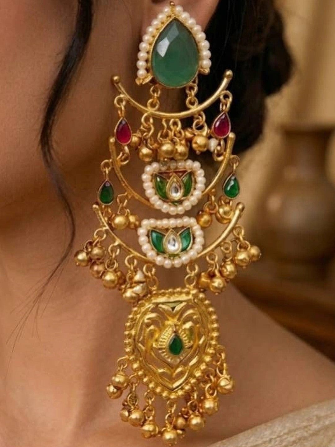 Close-up of kundan chandbali earring showing ruby drops, emerald stones, pearl borders and engraved gold pendant on a woman