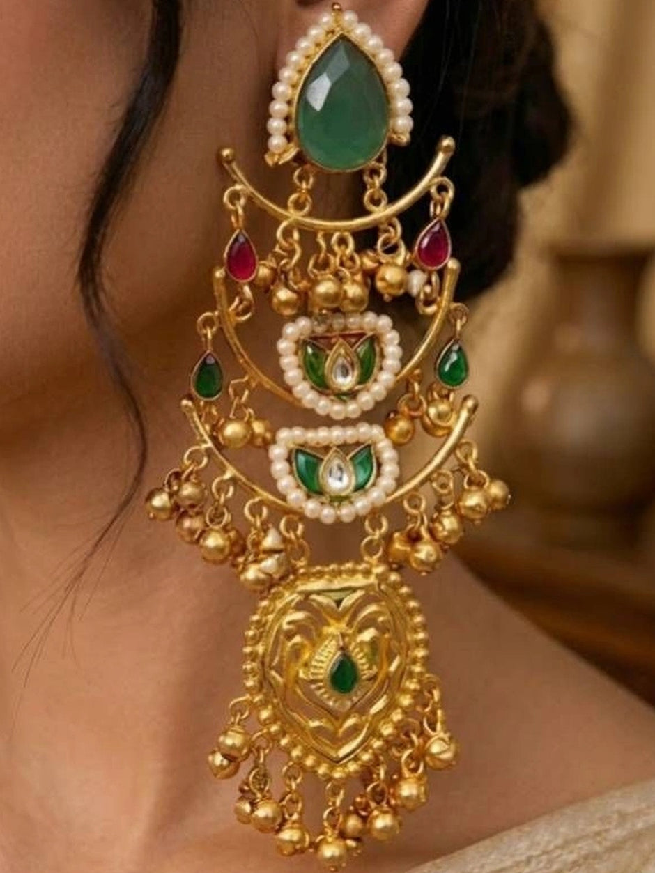 Close-up of kundan chandbali earring showing ruby drops, emerald stones, pearl borders and engraved gold pendant on a woman