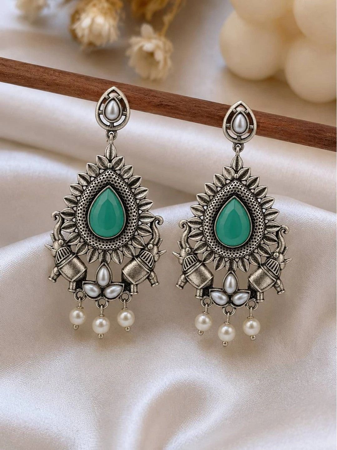 Pair of oxidised silver chandbali earrings with green teardrop stone and pearl drops on white fabric