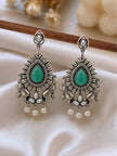 Pair of oxidised silver chandbali earrings with green teardrop stone and pearl drops on white fabric