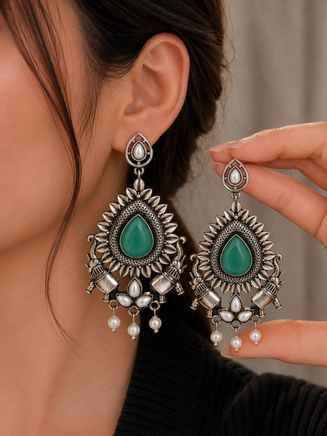 Model wearing oxidised silver green stone chandbali earring with second earring held up in hand