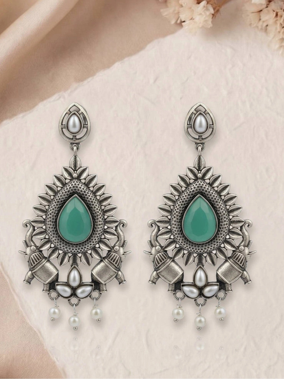 Pair of oxidised silver chandbali earrings with green stone and pearl bead drops on textured paper surface
