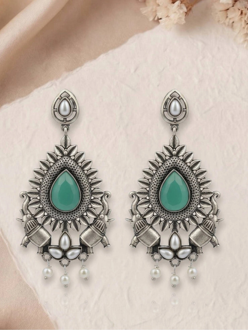 Pair of oxidised silver chandbali earrings with green stone and pearl bead drops on textured paper surface