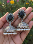 Close-up of two oxidised silver black stone jhumka earrings resting on an open palm outdoors