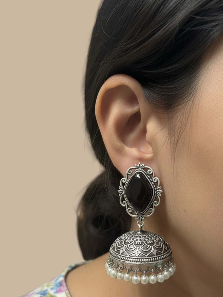 Oxidised silver jhumka earring with black stone stud worn on a woman's ear, side profile view