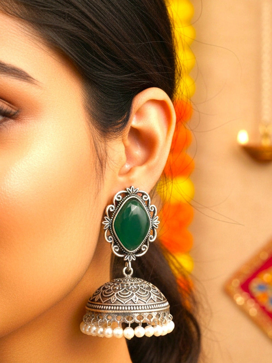 Woman wearing an oxidised silver green stone jhumka earring with floral marigold decor in the background