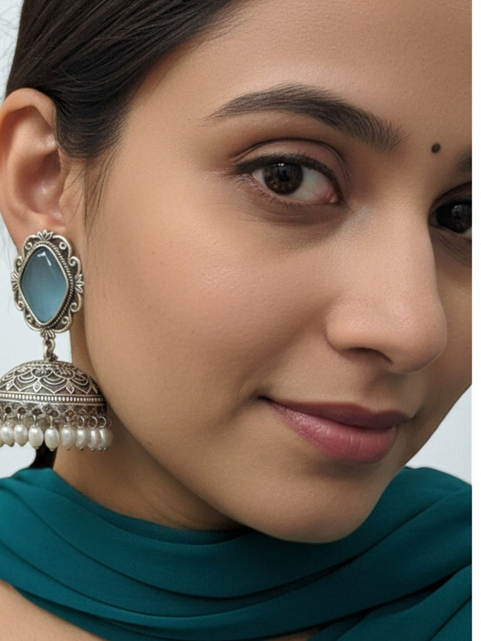 Close-up of oxidised silver jhumka earring worn on a woman's ear, shown with a teal outfit and a small bindi