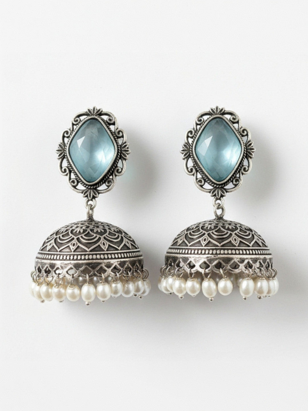 Flat lay of both oxidised silver jhumka earrings with blue faceted stone tops and ivory pearl drops on a white background