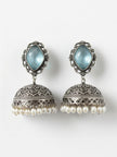 Flat lay of both oxidised silver jhumka earrings with blue faceted stone tops and ivory pearl drops on a white background