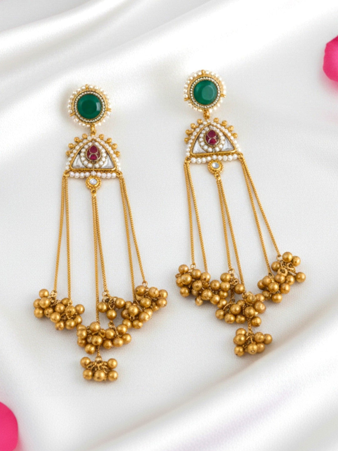 Pair of gold-plated kundan chandbali earrings with emerald stone tops and ghungroo bead drops on white satin