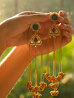 Hand holding two gold-plated kundan chandbali earrings with long chain and ghungroo clusters in warm sunlight