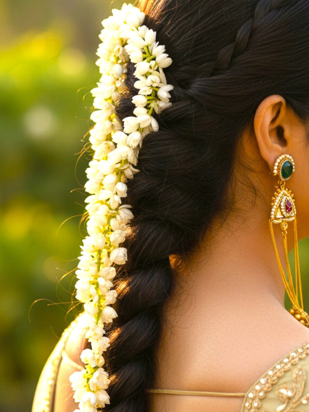 Gold-plated kundan chandbali earring worn by a woman with jasmine-adorned braid and gold saree blouse