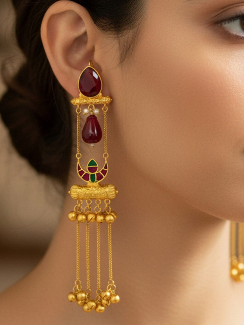 Gold-plated long tassel jhumka with ruby glass drop worn on a woman's ear, showing full length