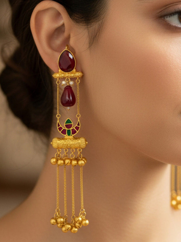 Gold-plated long tassel jhumka with ruby glass drop worn on a woman's ear, showing full length