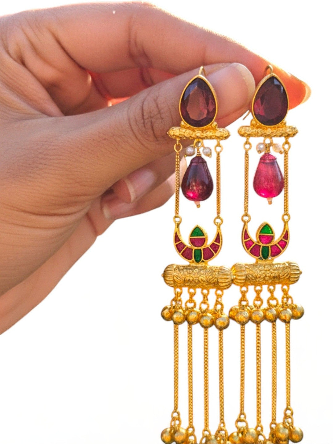 Pair of gold-plated ruby glass tassel jhumkas held in hand against white background